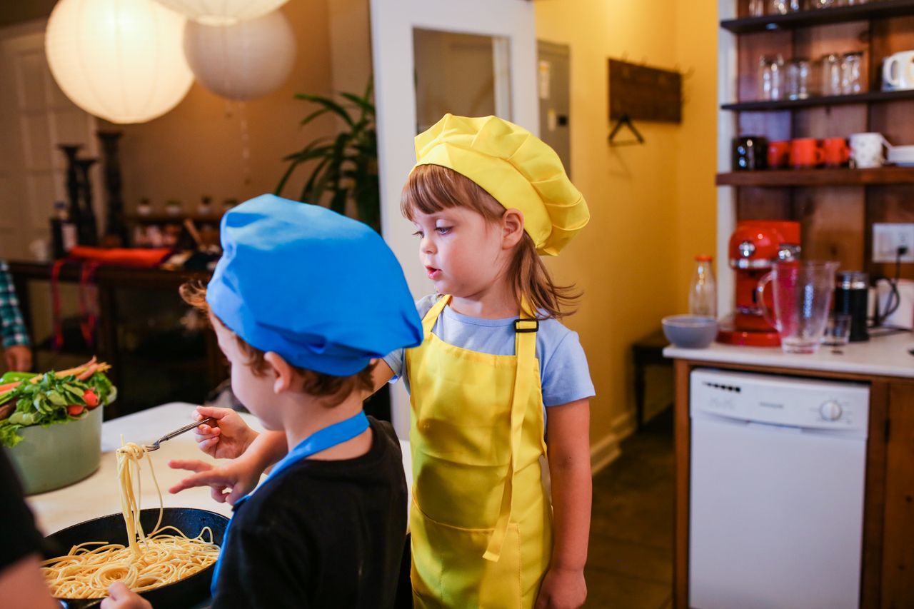 contact-img Two children in chef hats are cooking pasta together, enjoying a fun culinary experience.