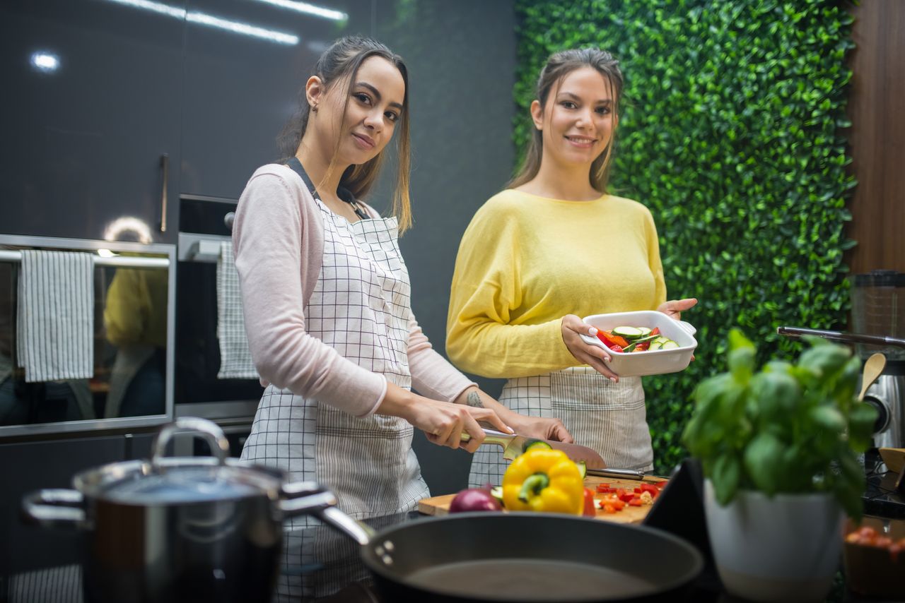 Two women cooking together with fresh vegetables in a contemporary kitchen setting.