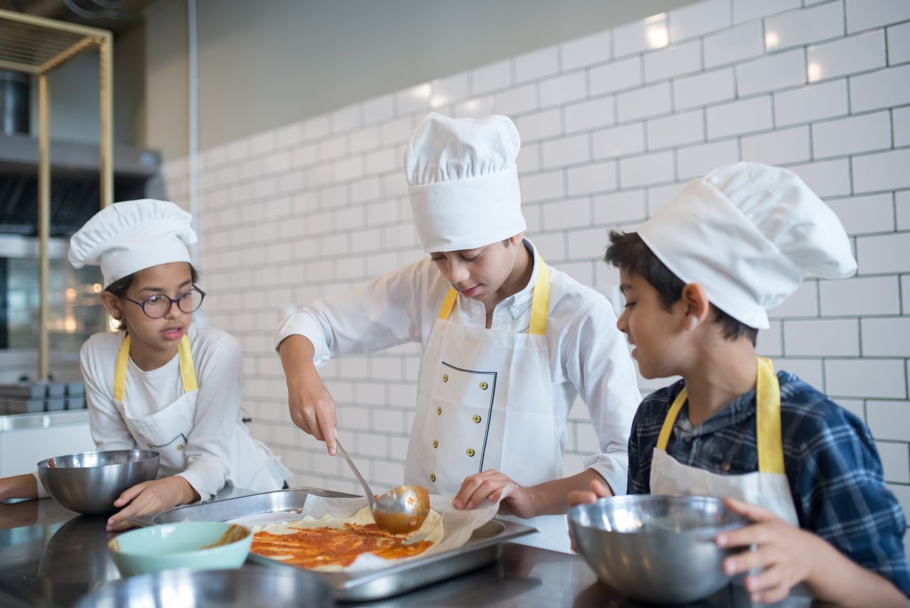 about-img-01 Young aspiring chefs in Portugal make pizza, spreading tomato sauce enthusiastically in a fun cooking class.