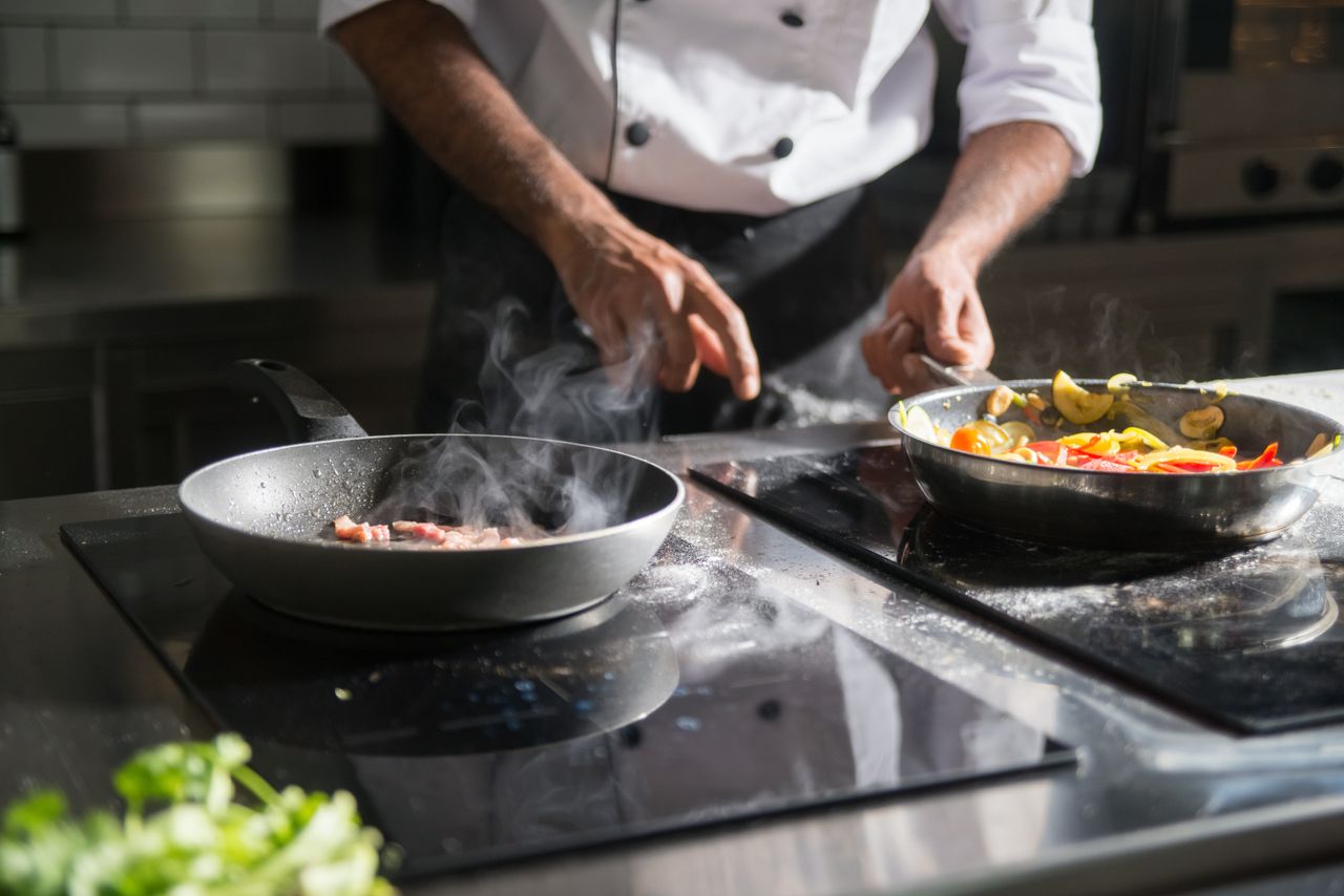 home-img A chef skillfully prepares a meal with fresh ingredients on an electric stove, emphasizing culinary expertise.