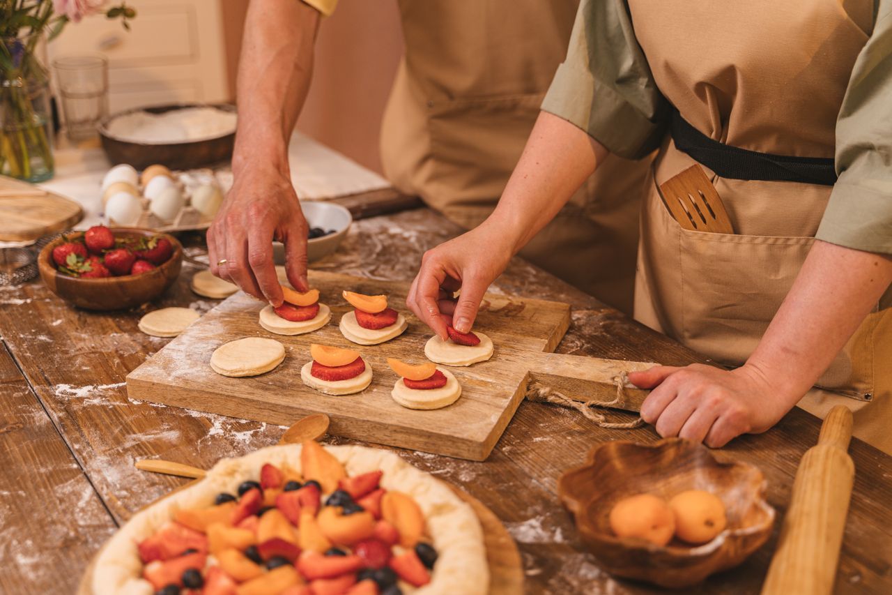Home Two chefs arrange sliced fruit on pastry dough for baking. Hands-on cooking in a cozy kitchen.