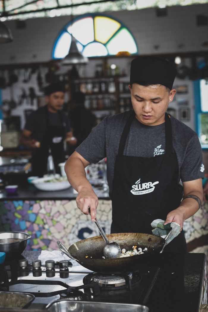 Mastering the First Impression: Your intriguing post title goes here An Asian chef diligently cooking in a restaurant kitchen, wearing a hat and apron.